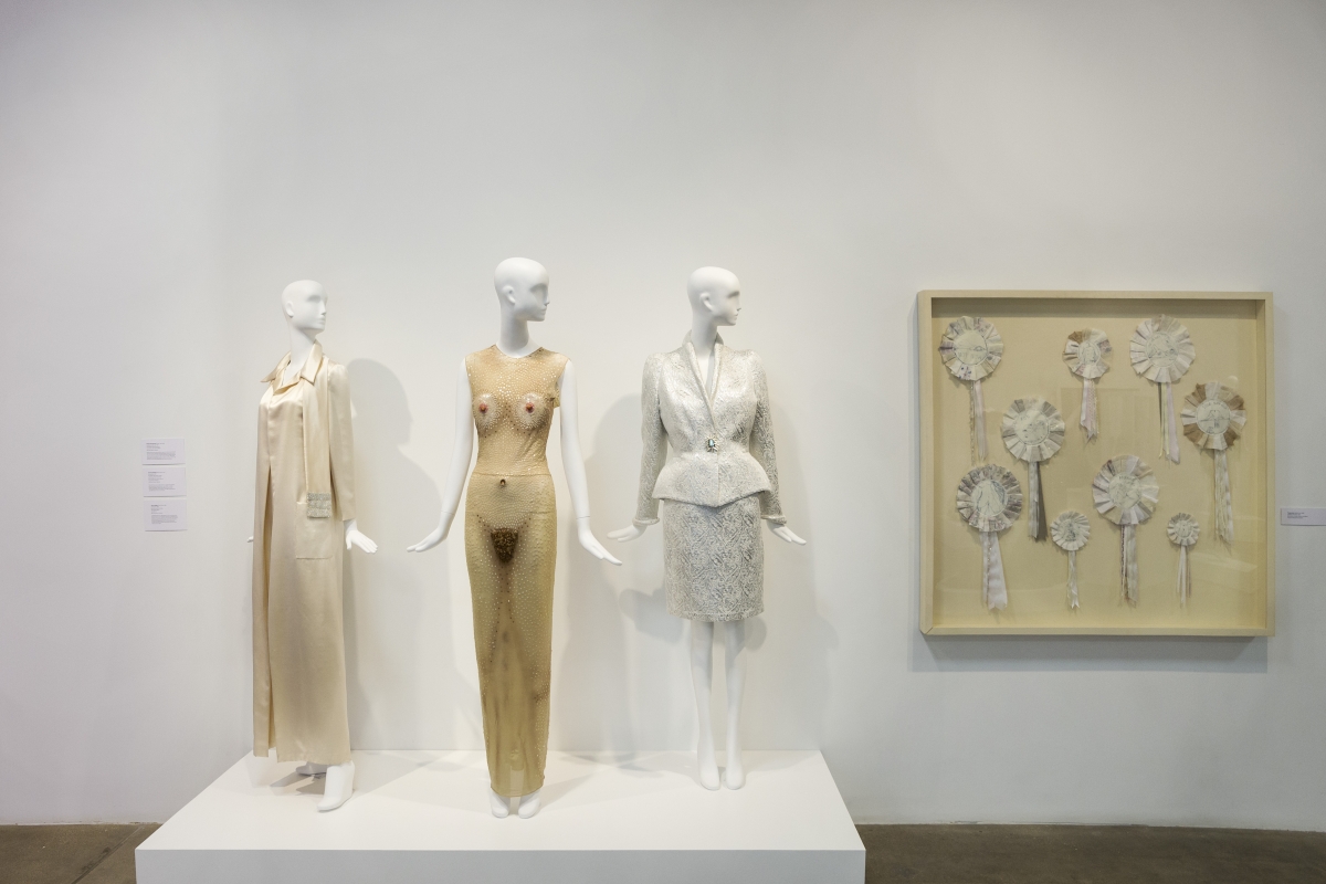 Three high fashion ensembles on mannequins next to framed Tracy Emin artwork