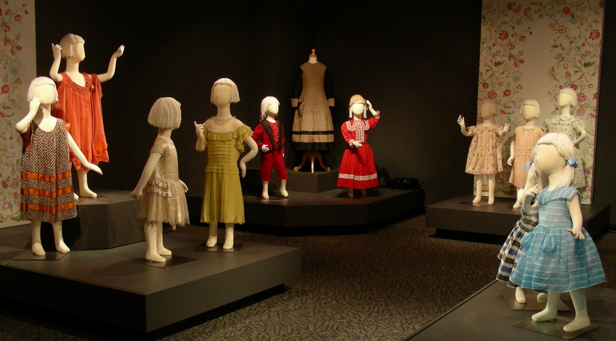 12 small mannequins showcasing children's fashions in gallery with floral backdrops