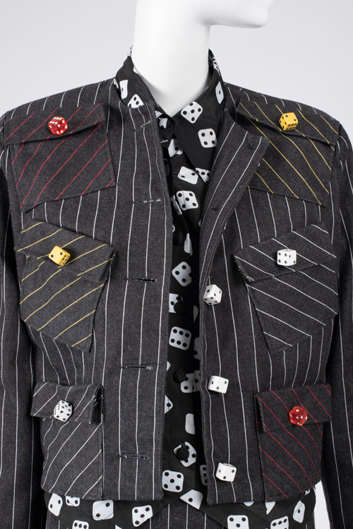 Detail of boxy black pinstripe jacket with randomly placed pockets and colorful dice buttons and blo